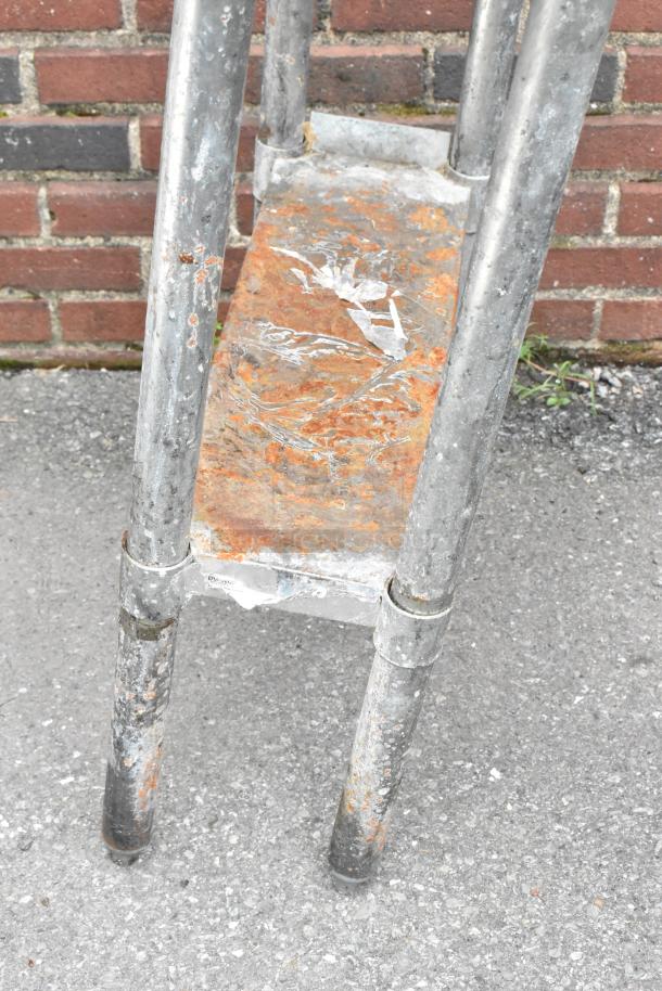 Stainless steel table with undershelf, showing rust and wear, standing on concrete. Suitable for restoration.