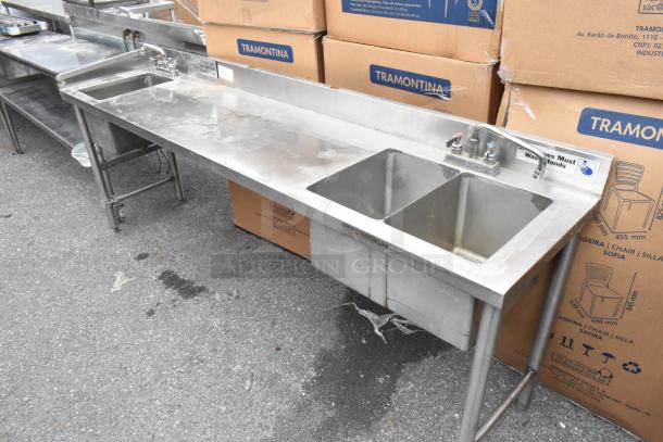 Stainless steel table with a single bay and two bay sink, industrial design, signs of use, includes faucet and fittings.