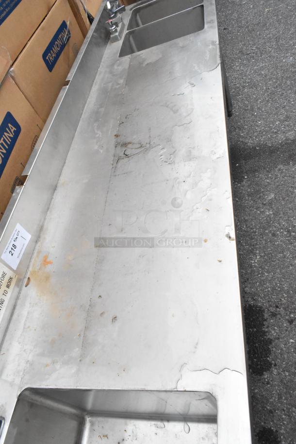 Stainless steel table with single bay and double bay sinks, showing minor wear. Auction tag reads "218".