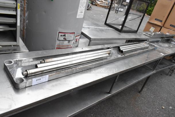 Metal shelf components on a stainless steel countertop, showing pipes and brackets. Number label "219" attached. Used condition.