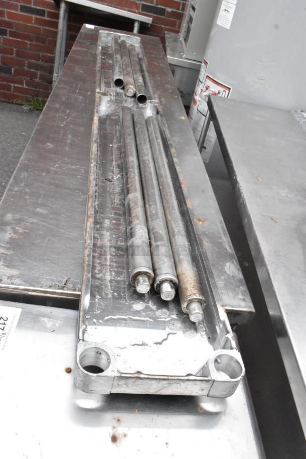 Metal shelf parts on a stainless steel surface, showing rust and wear, includes cylindrical rods and mounting components.