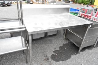 Stainless steel table with backsplash, industrial design, used condition, sturdy construction, ideal for kitchen or workshop.