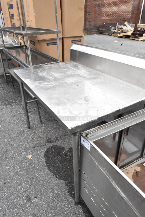 Stainless steel table with backsplash, showing signs of wear, sturdy legs, item number 222 visible.