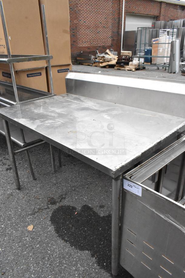 Stainless steel table with back splash, 4 sturdy legs. Slight surface wear, ideal for kitchen or industrial use, tag reading "222."