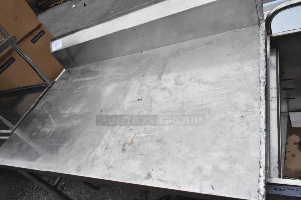 Stainless steel table with back splash, used condition, visible surface wear, ideal for kitchen or industrial use.