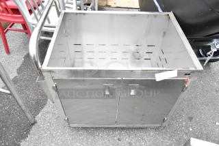 Stainless steel cart with commercial casters, open top, dual front doors, built-in handles, minor wear visible.