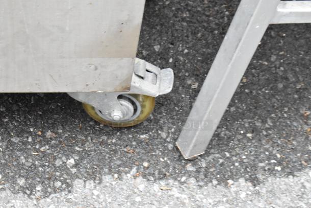 Stainless steel cart with commercial casters, showing a focus on the wheel and base. Slight wear visible.