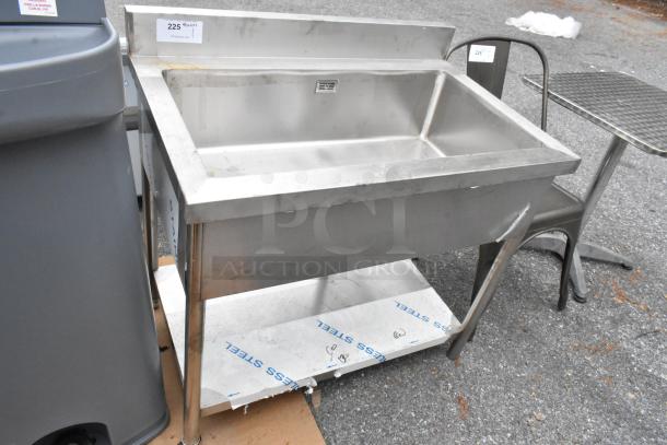 Stainless steel sink bay with under shelf. Features durable construction and visible wear. Includes rear backsplash.