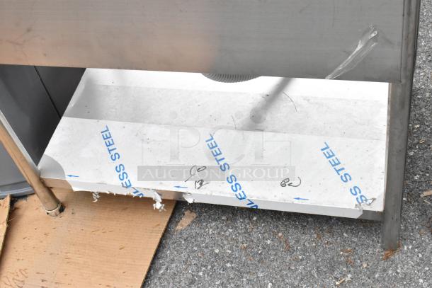 Stainless steel sink bay with under shelf, protective film partially intact, signs of light wear, suitable for commercial use.