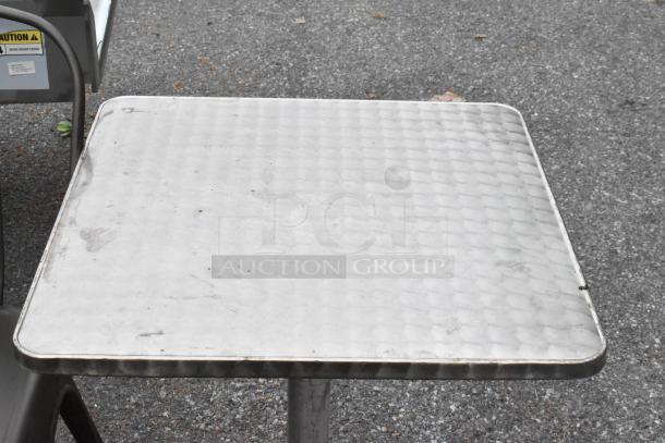 Gray metal Tolix style chair and chrome finish dining height table. Both are outdoor items with some visible wear.