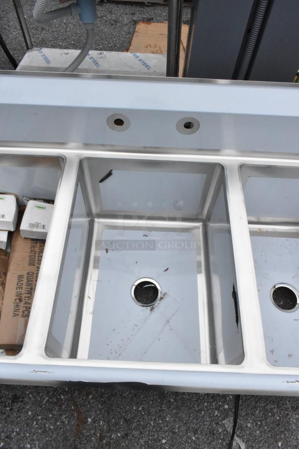 Brand new Regency 600S31824218 stainless steel 3 bay sink with dual drain boards, visible minor scratches and dents.