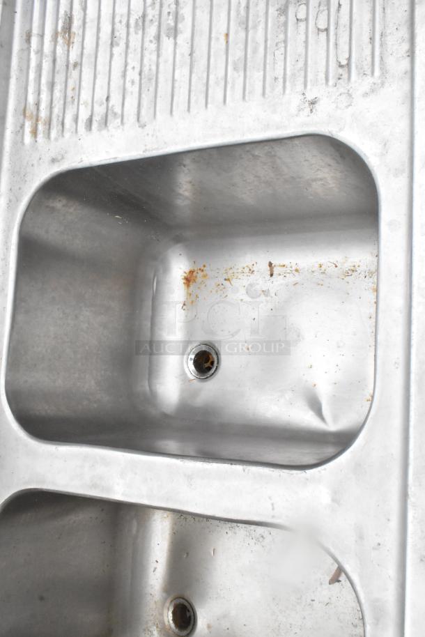 Stainless steel 3 bay bar sink with dual drain boards. Includes faucets and handles. Some visible rust and wear.