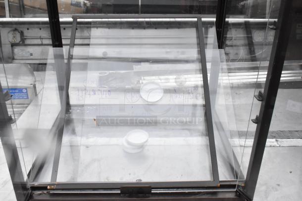Metal countertop dry display case merchandiser, clear glass panels, black metal frame, used condition, minor scuffs visible.