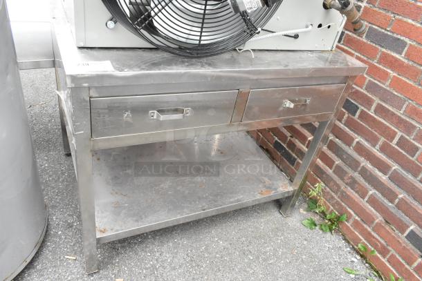Stainless steel table with two drawers and under shelf. Slight surface wear; sturdy construction ideal for commercial use.