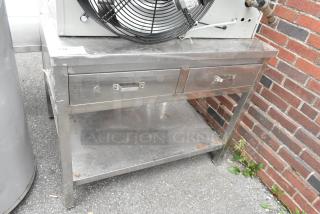 Stainless steel table with two drawers and under shelf. Slight surface wear; sturdy construction ideal for commercial use.