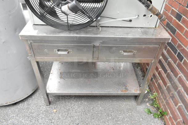 Stainless steel table with two drawers and under shelf, showing signs of wear and surface rust. Ideal for industrial use.