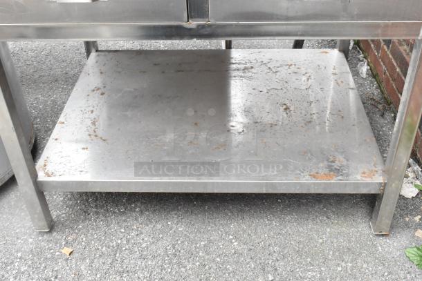 Stainless steel table with two drawers and an under shelf, showing surface wear and rust spots. Ideal for heavy-duty use.