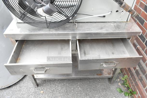 Stainless steel table with two open drawers and an under shelf. Surface shows signs of use.