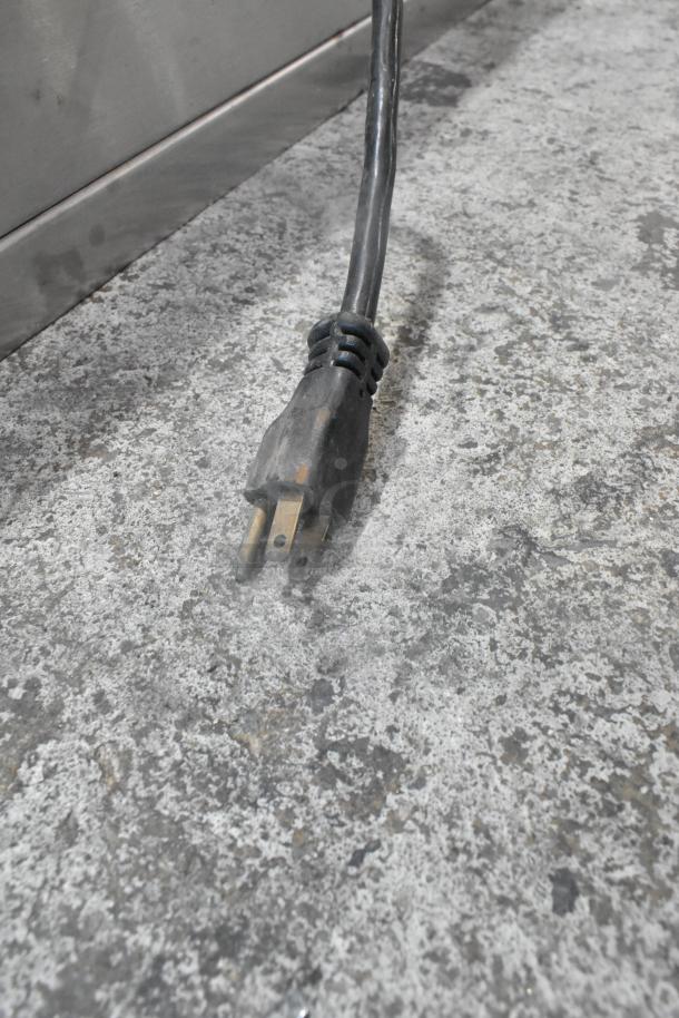 Sodir stainless steel commercial warming cabinet power cord, 115 volts, showing plug on stone floor background.