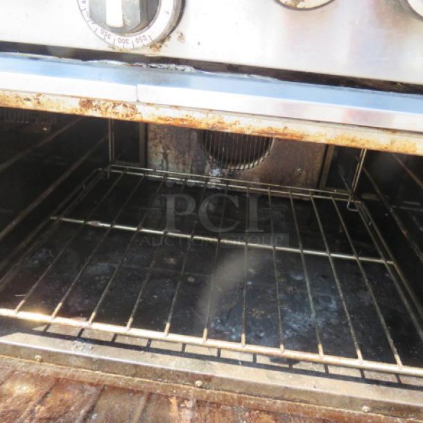 Garland 10 burner natural gas range, used condition, features two racks and a stainless steel overshelf on casters.