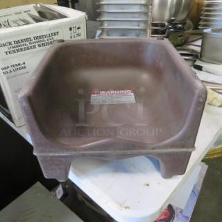 Brown booster seat, plastic material, slight wear. Warning label on seat surface. Measures approximately 15x15 inches.
