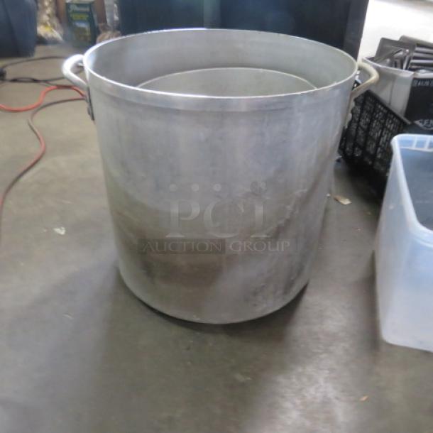 Large aluminum stock pot, 18x18 inches, with dual handles. Shows signs of use, suitable for commercial cooking.