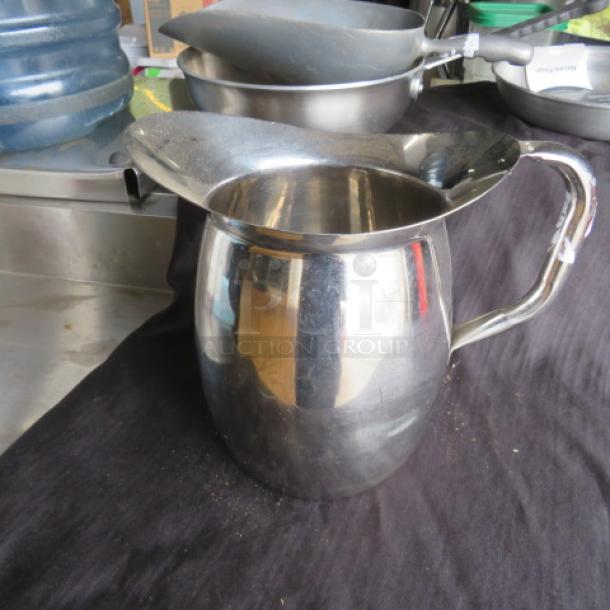 Stainless steel pitcher with a curved handle and wide spout, in good condition, reflecting surroundings.