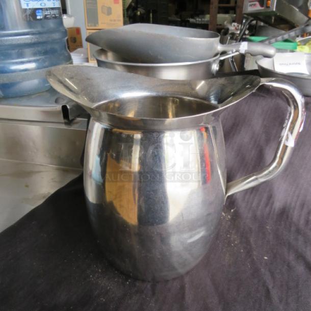 Stainless steel pitcher, shiny finish, wide spout, ergonomic handle, good condition, no visible markings or labels.