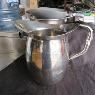 Stainless steel pitcher, shiny finish, wide spout, ergonomic handle, good condition, no visible markings or labels.