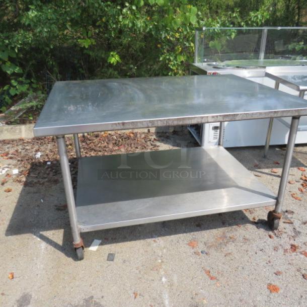 Stainless steel table with under shelf on casters, 60x45x36 inches. Used condition with visible wear. Suitable for commercial use.