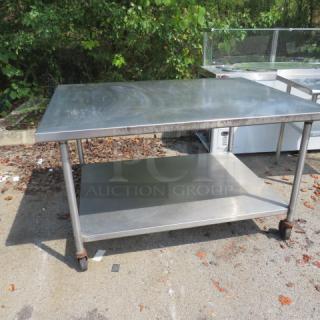 Stainless steel table with under shelf on casters, 60x45x36 inches. Used condition with visible wear. Suitable for commercial use.