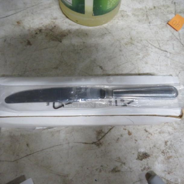 One dozen new solid handle knives, stainless steel, individually wrapped in a white box. Pristine condition.
