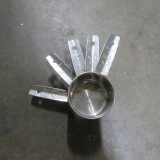 New set of stainless steel measuring cups, with engraved measurements, fanned display on a dark surface.
