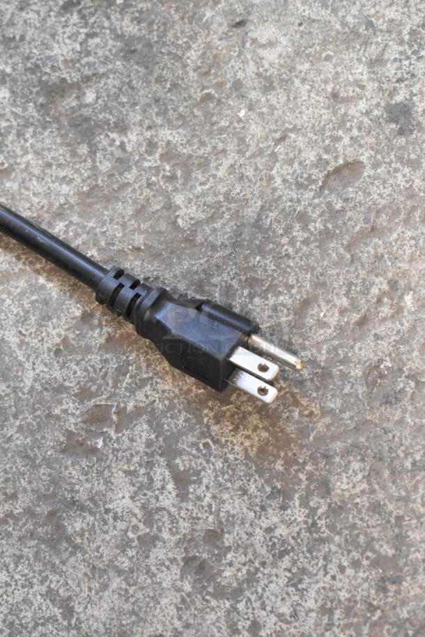 Close-up image of a black electric plug on a textured concrete surface. Plug has three prongs.