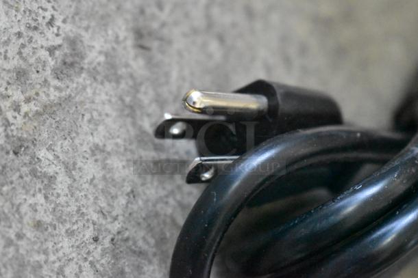 Close-up of a power plug for the Crathco D25-4 beverage dispenser, showing three metal prongs against a gray background.