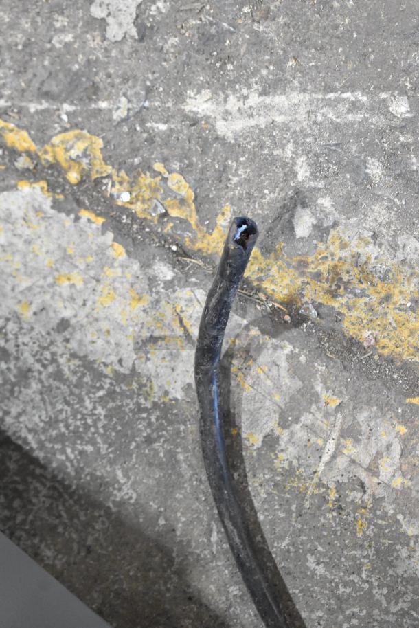 An image of a damaged power cord on a rough, speckled concrete surface with yellow paint markings.