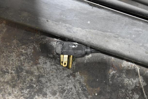 A close-up of a power plug for the True T-35 cooler on a textured floor. Plug shows wear, indicating prior use.