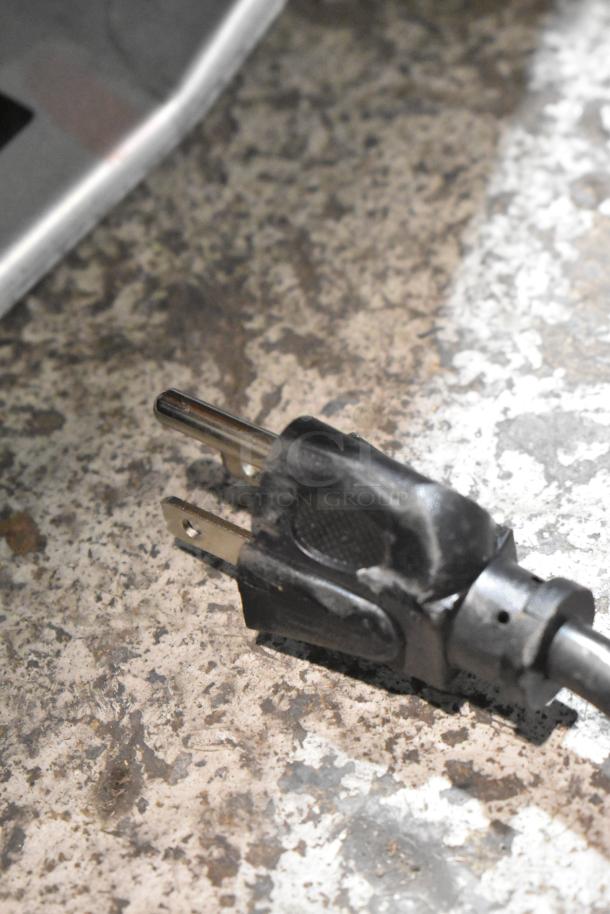 A close-up view of a power plug on a textured surface, part of the Galanz GLR31TS1E02 mini cooler with freezer.