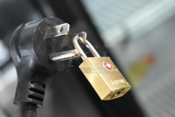 Power plug of True GDM-26-HC cooler secured with a brass padlock, showing safety measures for device use.