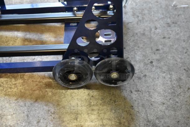 Metal dolly with sturdy frame and two large wheels on smooth surface. The blue structure features circular cutouts and metal rails.
