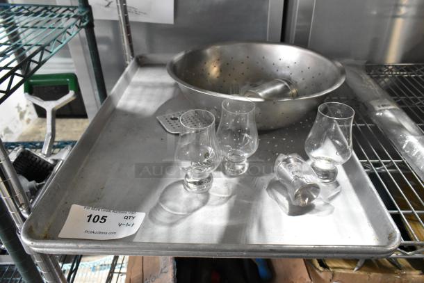 Lot of assorted items including a metal colander, glassware, and baking pan on a shelf. Item label reads "105 QTY V-lot."