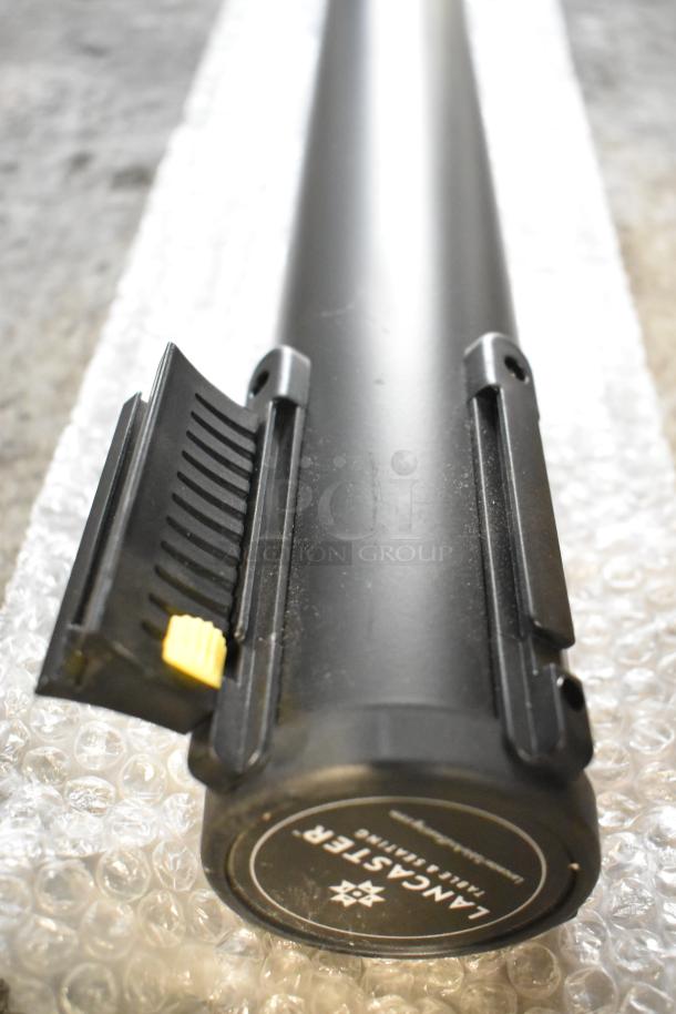 Lancaster Table & Seating Stanchion Post, black, sturdy design, retractable belt latch, circular base with brand label visible.