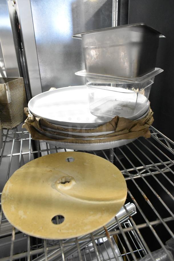 Auction lot featuring a food processor continuous feed head, Dormont gas hoses, and ceramic plates on metal shelves.