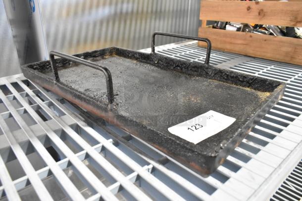Rugged metal tray with dual handles, showing wear and surface texture. Label with "123 QTY" visible on corner.