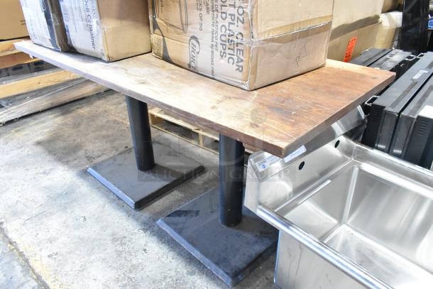 Wooden table with visible grain mounted on two sturdy black metal bases. Used condition with some wear on the surface.