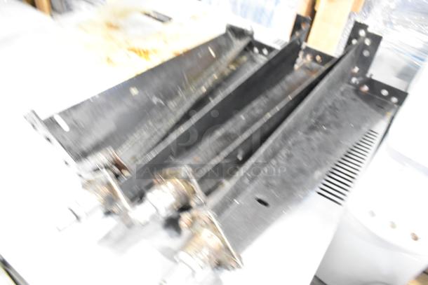 Blurry image of metal components, possibly parts of a commercial oven, lacking visible details or labels.