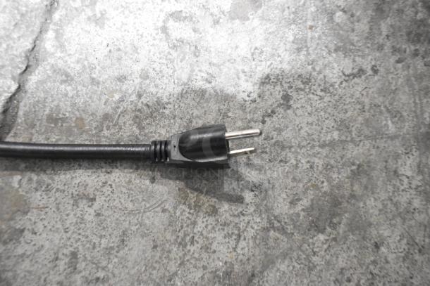 The image shows a power plug for the Winco FW-S600 electric food warmer, set on a concrete surface.