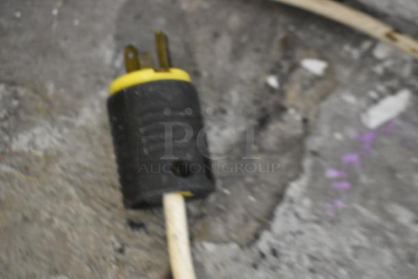Close-up of a plug from Caravell 406-995 Chest Freezer Merchandiser. Black and yellow plug on a concrete floor.
