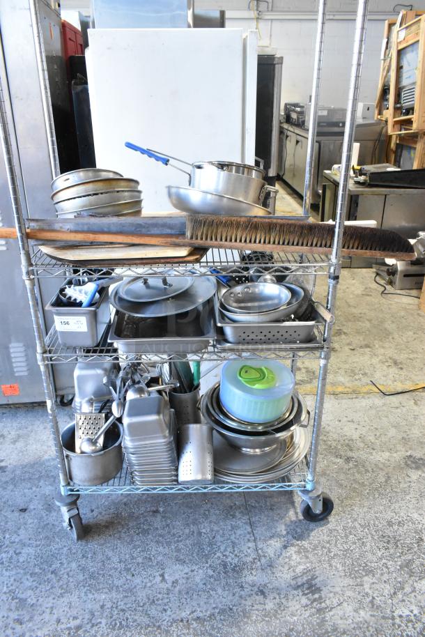 Three-tier cart with wooden pizza peels, stainless steel bins, skillets, round baking pans. Various kitchenware in used condition.