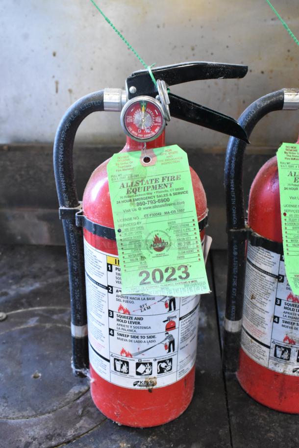 Two Kidde fire extinguishers with inspection tags. Red, tagged for 2023, pressure gauge visible, pickup only.